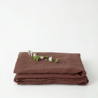 Folded chocolate brown linen flat sheet with a small branch on a white background 